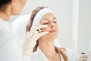 A woman with her eyes closed is receiving an injection in her cheek from a physician.